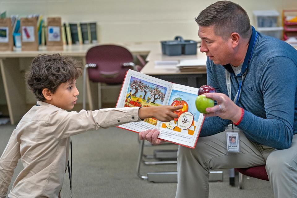 Aser Aasem, lef, asks his teacher, Ben Danner, a question as students study apples by reading a non-fiction book at Jeremiah Gray Elementary School, Tuesday, Oct. 10, 2023 during Fall break intercession classes. Perry Township school district has a 2-week break with the classes which help kids catch up on classwork during the break.