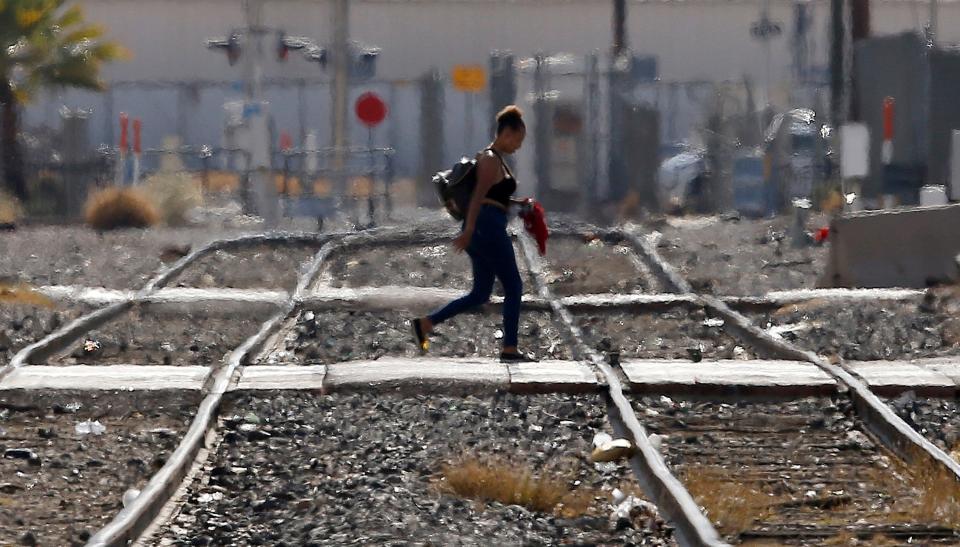 While the heat waves rise up from the ground, a woman crosses the railroad tracks as temperatures climb past 112 degrees on July 5, 2018, in Phoenix.