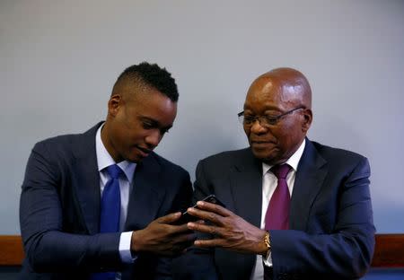 FILE PHOTO: Former South African president Jacob Zuma hands a mobile phone to his son Duduzane ahead of his appearance at the Specialised Commercial Crimes Court in Johannesburg, South Africa, January 24, 2019. REUTERS/Siphiwe Sibeko/File Photo