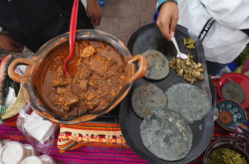 Un vendedor prepara un guiso de cerdo, a la izquierda, en la Feria de Comida Prehispánica en la delegación Iztapalapa de la Ciudad de México, el viernes 29 de julio de 2022. Iztapalapa, la delegación más grande de la Ciudad de México, lanzó la feria para rescatar y preservar la cocina tradicional mexicana. (AP Foto/Marco Ugarte)