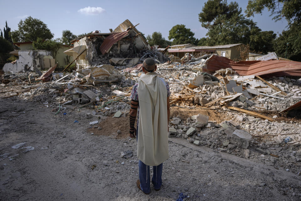 An Israeli man wearing a prayer shawl prays next to houses destroyed by Hamas militants in Kibbutz Be'eri, Israel, Sunday, Oct. 22, 2023. The kibbutz was overrun by Hamas militants from the nearby Gaza Strip on Oct.7, when they killed and captured many Israelis. (AP Photo/Ariel Schalit)