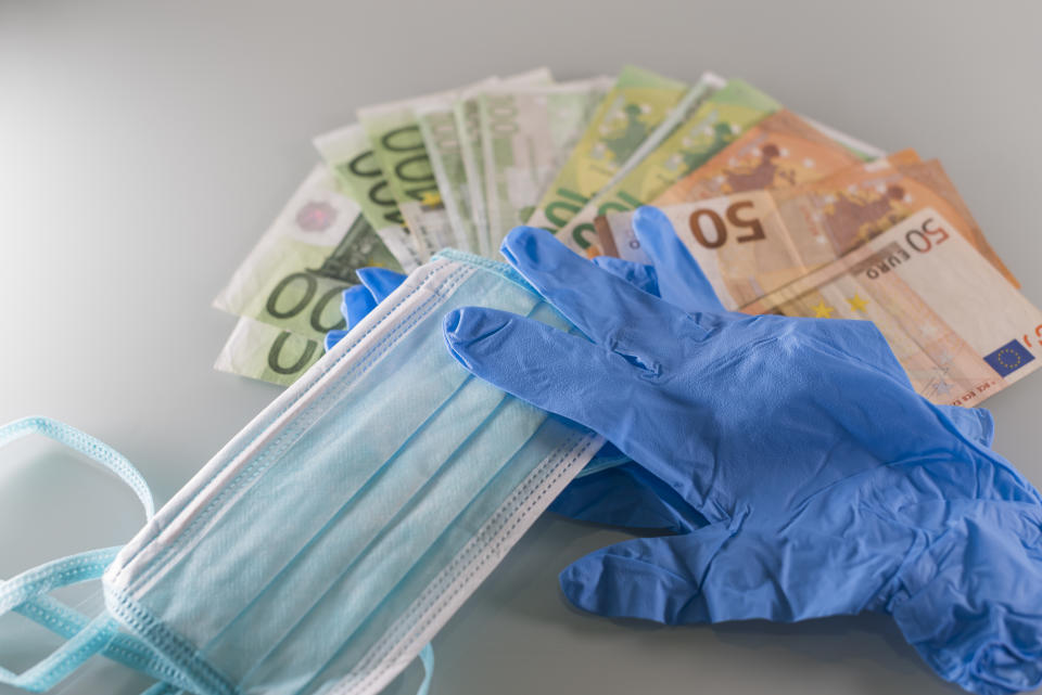 Una mascarilla quirúrgica al lado de unos guantes azules y una serie de billetes de 100 y 50 euros.