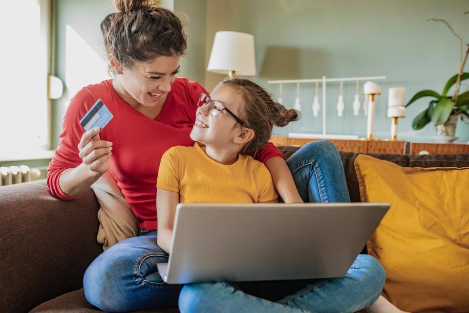 An adult and a child sitting on a couch shop online.