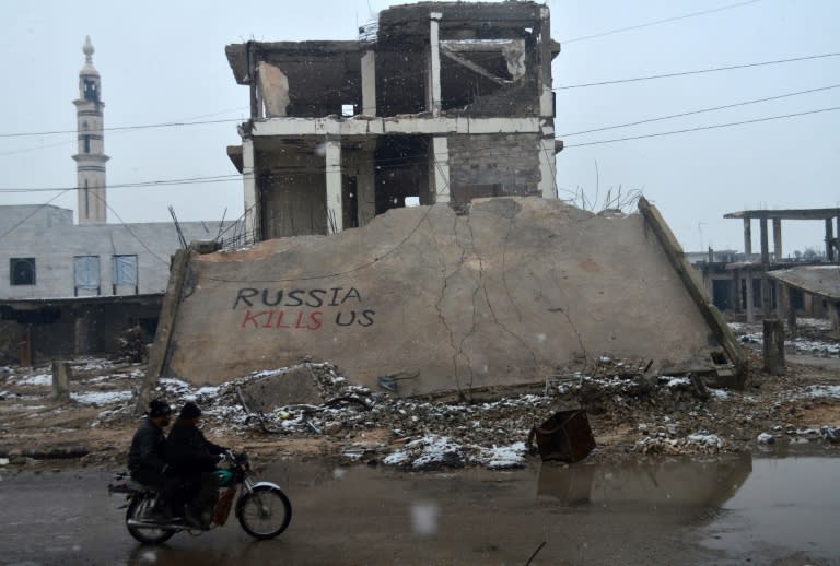 Syrians ride a motorbike past a collapsed building on which graffiti reads "Russia kills us" in the central Syrian town of Talbisseh in the Homs province on January 1, 2016