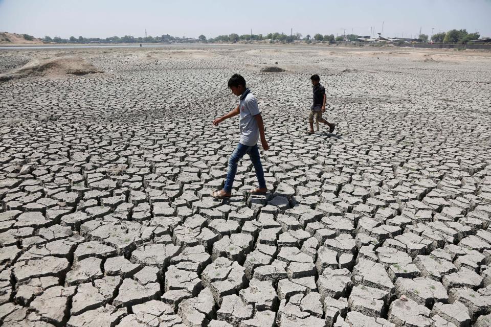 Indian boys on their way to play cricket walk through a dried patch of Chandola Lake in Ahmadabad, India, on May 14, 2016. In 2016, much of India suffered from a heat wave that lasted for weeks, along with a severe drought that has decimated crops, killed livestock and left at least 330 million Indians without enough water for their daily needs.