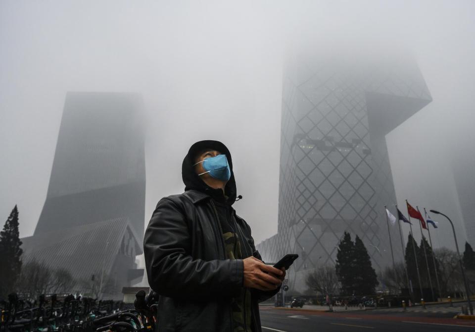 A Chinese man wears a protective mask as he stands near the CCTV building in fog and pollution during rush hour in Beijing (Getty Images)