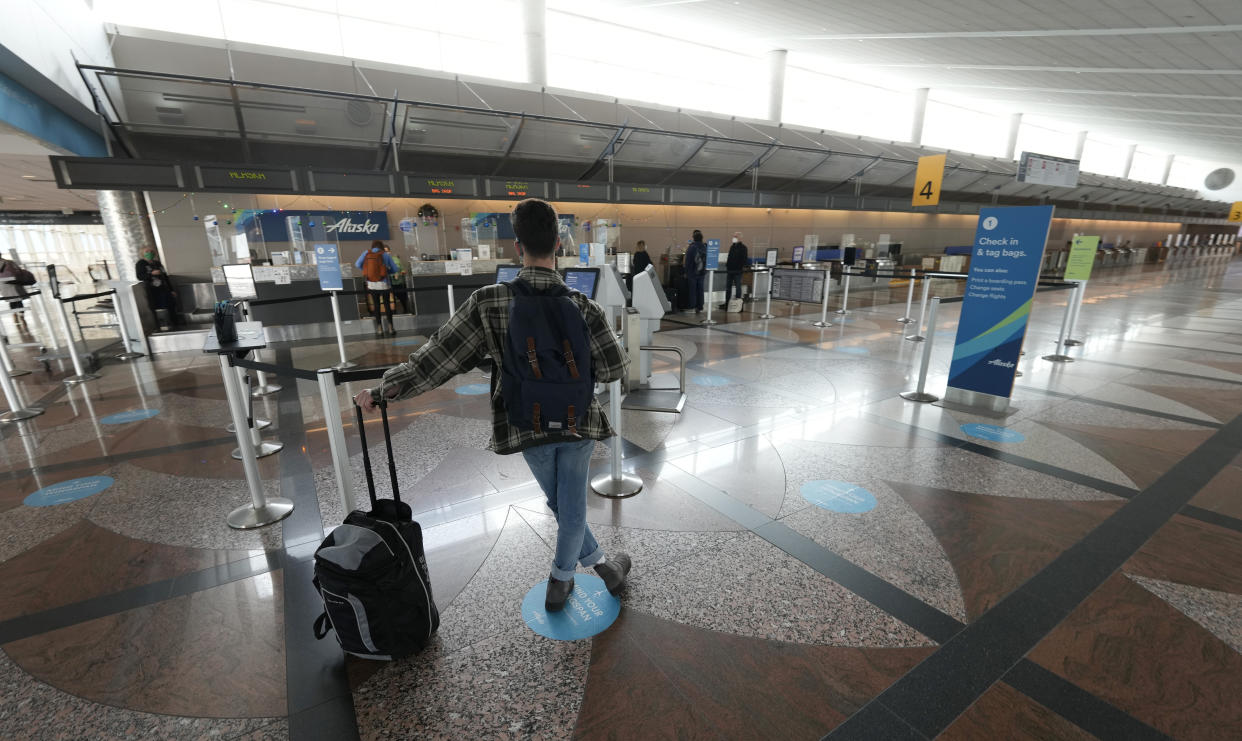 FILE - A lone traveler waits at the check-in counter for Alaska Airlines in the terminal of Denver International Airport on Dec. 24, 2021, in Denver. Alaska Airlines said Thursday, Jan. 6, 2022, it will trim its schedule by about 10% for the rest of January at it deals with “unprecedented” numbers of employees calling in sick during the current COVID-19 surge. (AP Photo/David Zalubowski, File)