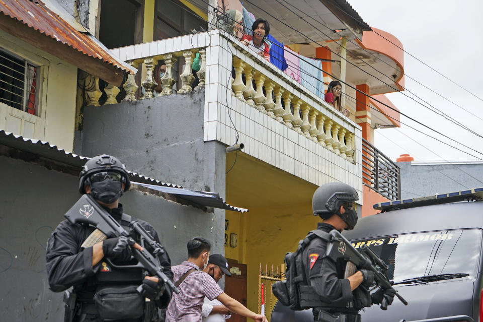 Residents look on as police officers stand guard during a raid on a house that, police believe, is linked to the suicide bombers of Sunday's church attack, in Makassar, South Sulawesi, Indonesia, Monday, March 29, 2021. Two attackers believed to be members of a militant network that pledged allegiance to the Islamic State group blew themselves up outside the packed Roman Catholic cathedral during a Palm Sunday Mass on Indonesia's Sulawesi island, wounding a number of people, police said. (AP Photo/Daeng Mansur)