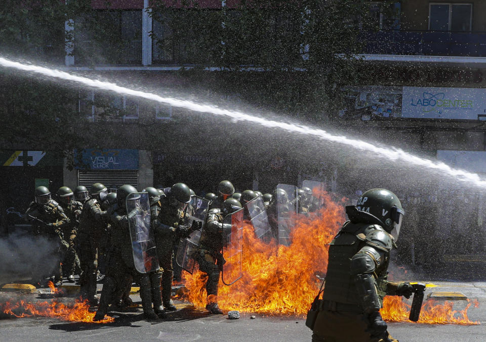 Una bomba molotov explota frente a la policía mientras un vehículo lanza agua a manifestantes que salieron a las calles en la tradicional marcha del Encuentro de dos Mundos, que recuerda el descubrimiento de América y la posterior conquista de los pueblos indígenas, en Santiago de Chile el lunes 12 de octubre de 2020. (AP Foto/Esteban Felix)