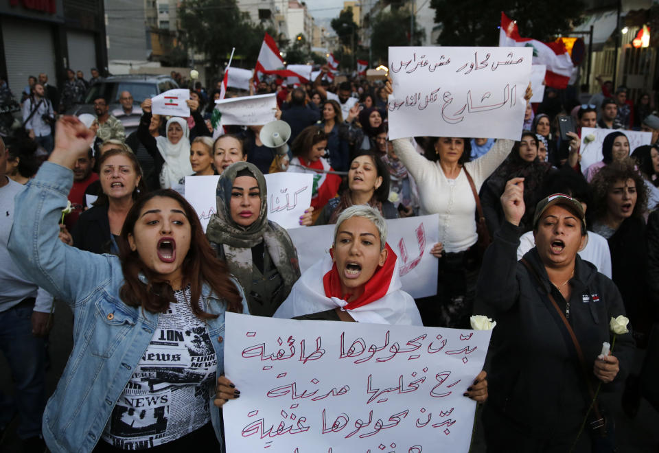 Lebanese women shout slogans, as they carry Arabic placards that read:"They want to turn it to sectarianism, we will keep it civil, they want to turn it violent and we will keep it peaceful," during a protest at a former Beirut frontline between Christian district of Ain el-Rummaneh and a Muslim Shiite district of Shiyah, in Beirut, Lebanon, Wednesday, Nov. 27, 2019. Hundreds of Lebanese women marched across a former front line in the Lebanese capital carrying white roses and Lebanese flags to denounce overnight clashes between rival groups that injured dozens of people. (AP Photo/Hussein Malla)