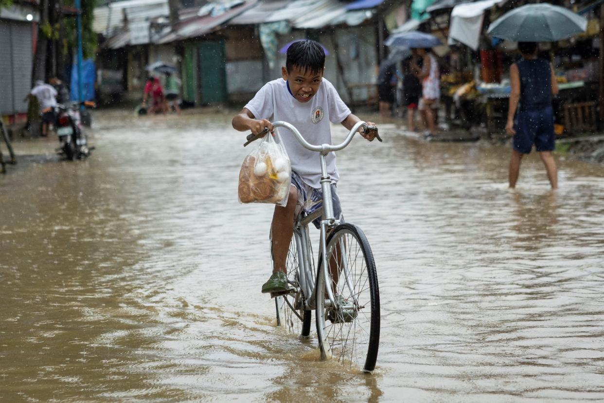 A boy carrying a plastic bag with bread and eggs, rides his bike through a flooded road after heavy rains brought by Tropical storm Yagi, locally known as Enteng, in Baras, Rizal province, Philippines, Sept. 2, 2024.