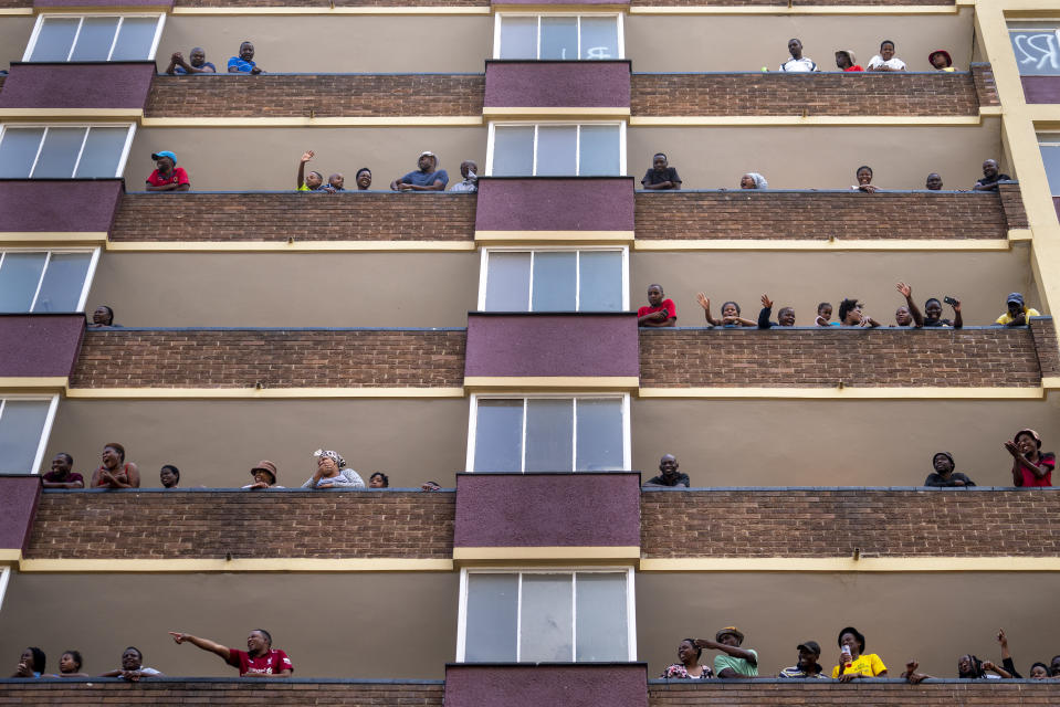 Residents of the densely populated Hillbrow neighborhood of downtown Johannesburg, confined in an attempt to prevent the spread coronavirus, stand and wave from their balconies, Friday, March 27, 2020. South Africa went into a nationwide lockdown for 21 days in an effort to mitigate the spread to the coronavirus. The new coronavirus causes mild or moderate symptoms for most people, but for some, especially older adults and people with existing health problems, it can cause more severe illness or death. (AP Photo/Jerome Delay)