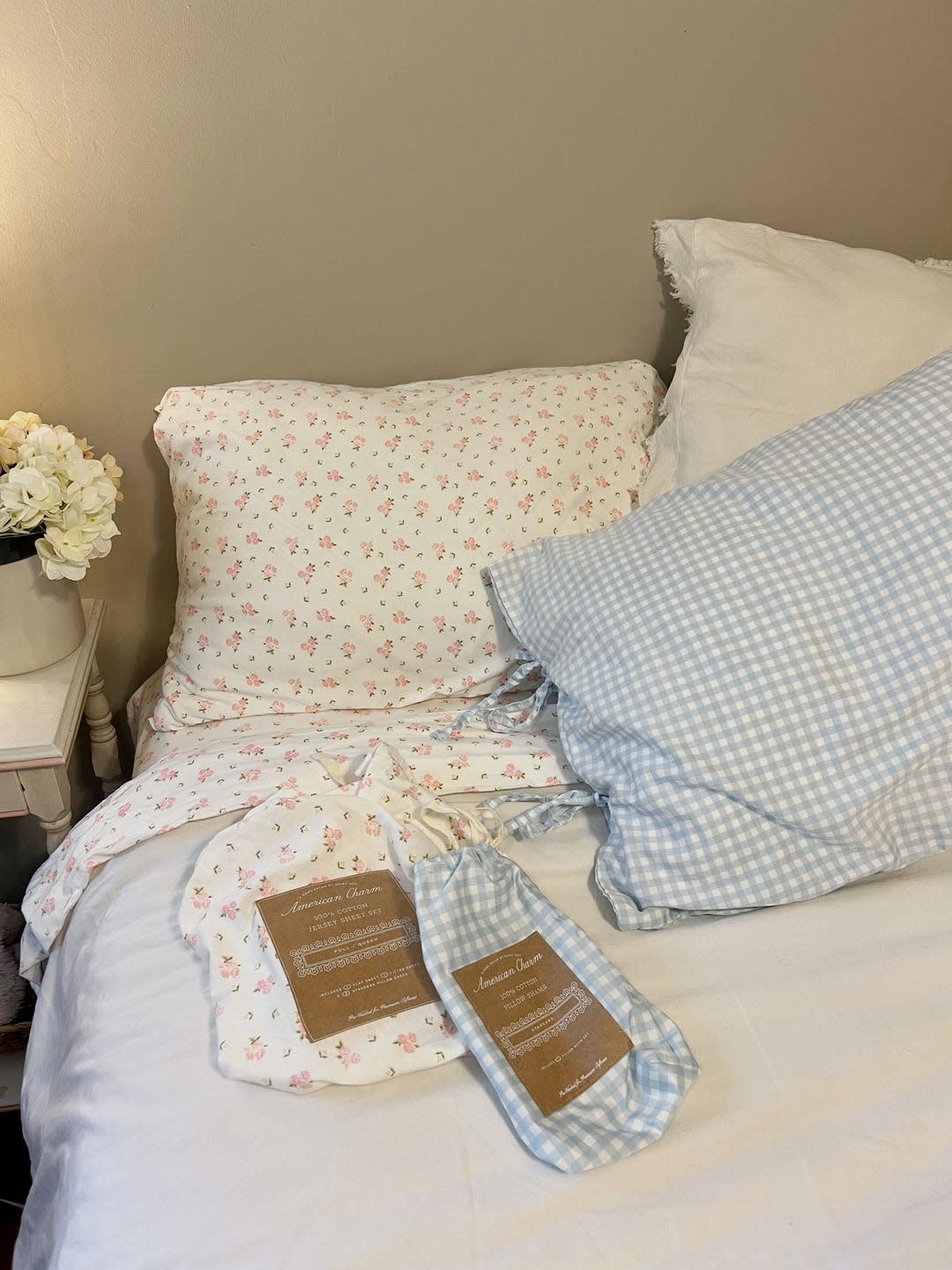 a white bed with floral sheets and a gingham pillow on it