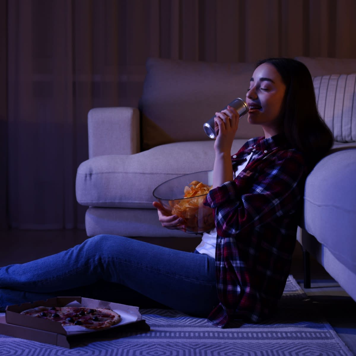 woman drinking from can and eating pizza at night