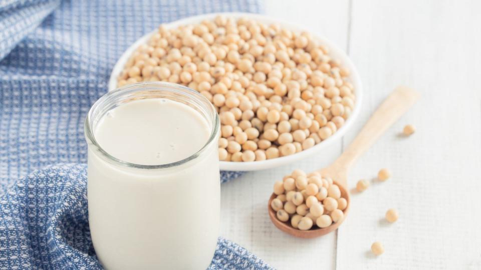 a glass of soy milk on a white wood floor with soybean as a background