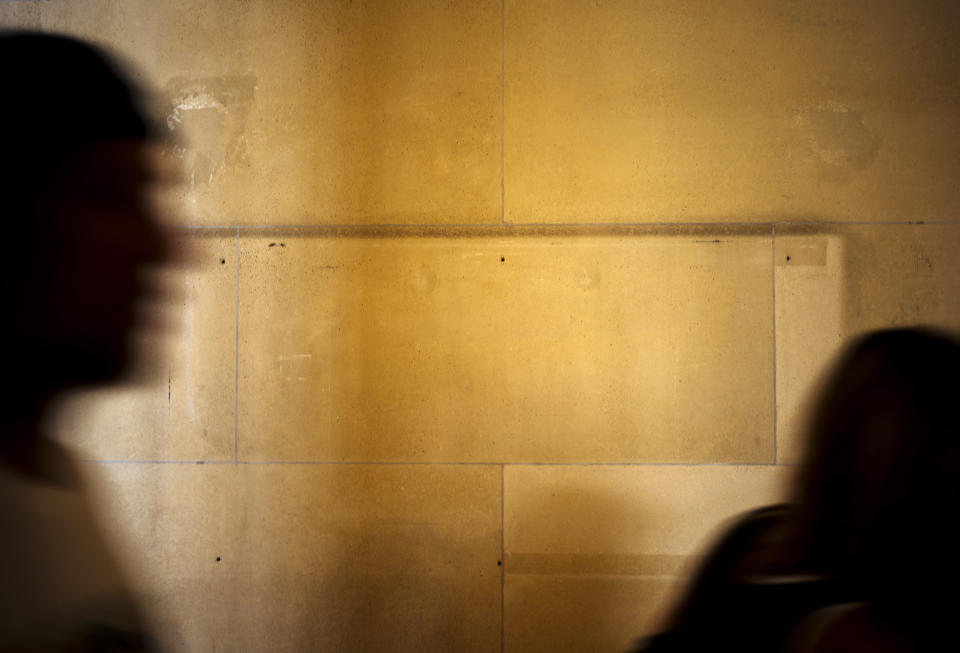 People walk past a wall where a sign with the list of donators has been removed at the Louvre Museum in Paris, France, Wednesday, July 17, 2019. France's Louvre museum has taped over the Sackler name as donors to a wing of the building after protests against the family blamed for the opioid crisis in the United States. (AP Photo/Kamil Zihnioglu)