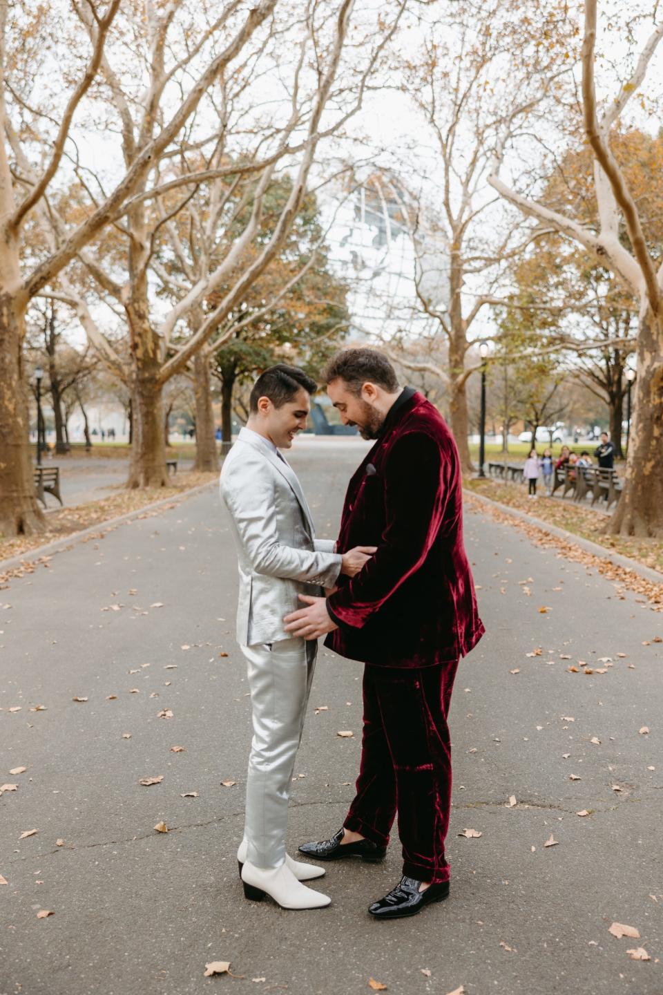 Two grooms embrace and look at each other's outfits.