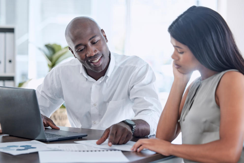 Businessman, black woman and documents in finance training, kpi data analysis and target audience research review with intern. Smile, happy and talking manager with laptop pointing at financial paper
