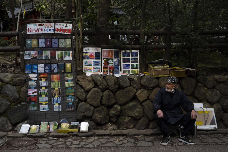 Artist Kinji Kimura, 76, who sells postcard-sized prints of work, sits on a stool while waiting for customers near the Arashiyama Bamboo Forest in Kyoto, Japan, March 18, 2020. "Arashiyama is empty," is a new catchphrase that appeared on posters in the area. "It's time to visit Kyoto," they say, because there are no long lines and waiting to do river rafting, get into popular temples or cross the bridge. (AP Photo/Jae C. Hong)