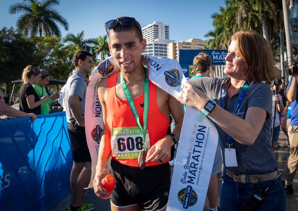 Jaelin Funk, the winner of the full-marathon, gets draped in the ribbon by race director Madeleine Ely at The Garden of Life Palm Beaches Marathon on Flagler Drive in West Palm Beach, Florida on December 12, 2021.