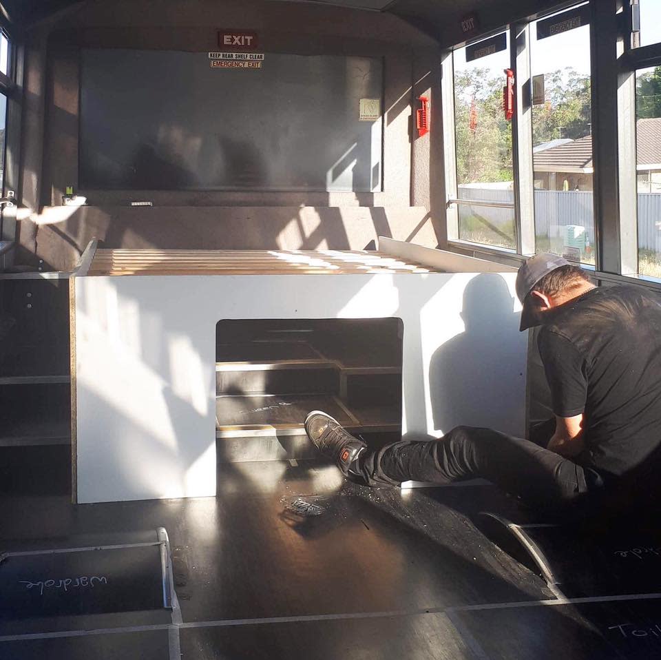 A man building a bed in the rear of the bus