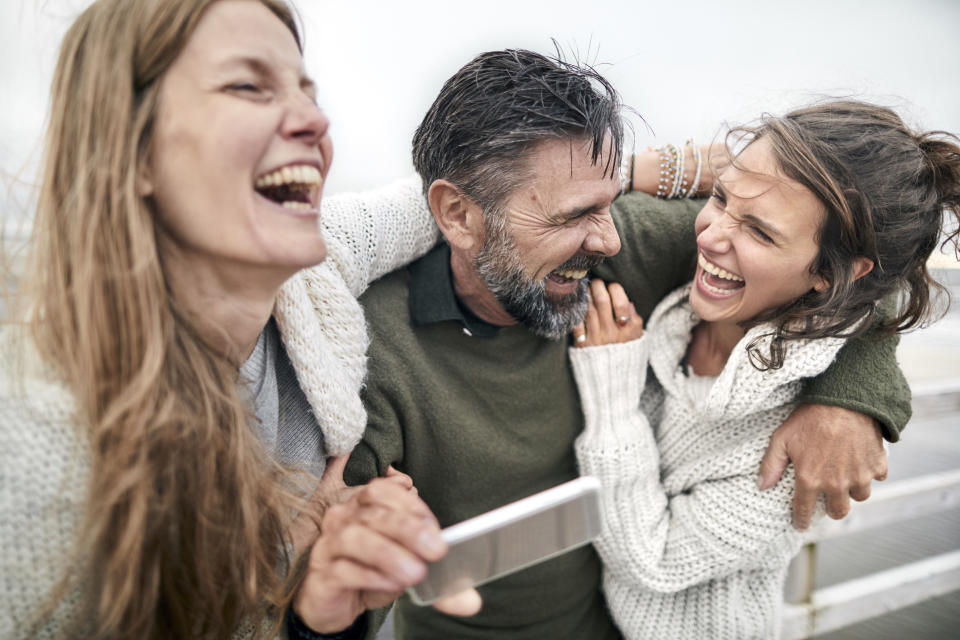 Laughing man and two women with smartphone by the sea