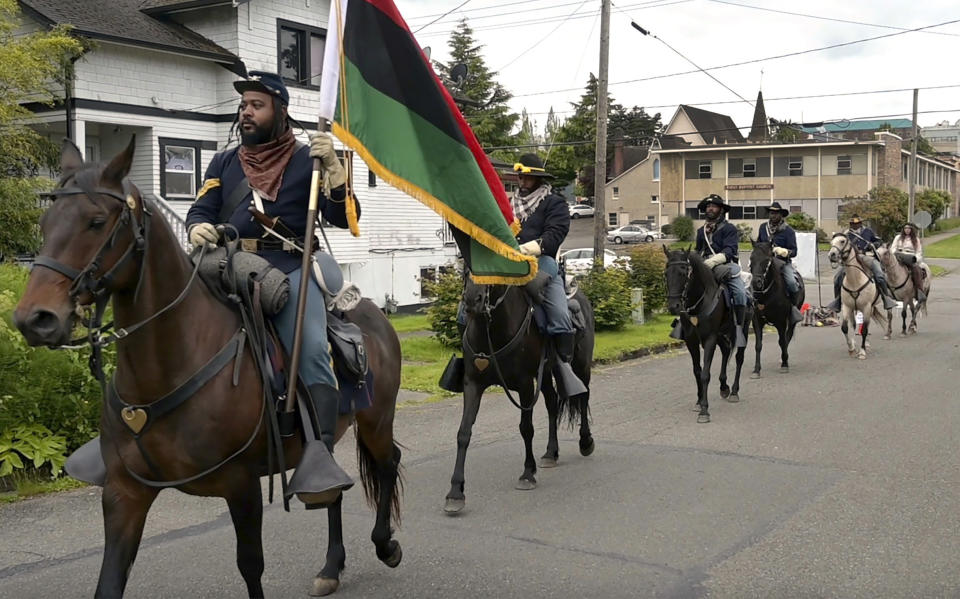 Mounted members of the Buffalo Soldiers of Seattle historical organization enter the Marketplace vendors' lane to open the Juneteenth Celebration Festival called Omo Africa, on Sunday, June 19, 2022, at Rebecca Howard Park in Olympia, Wash. (Steve Bloom/The Olympian via AP)