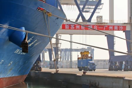 Crane lifts a container from a truck next to a cargo vessel at a port in Yantai, Shandong