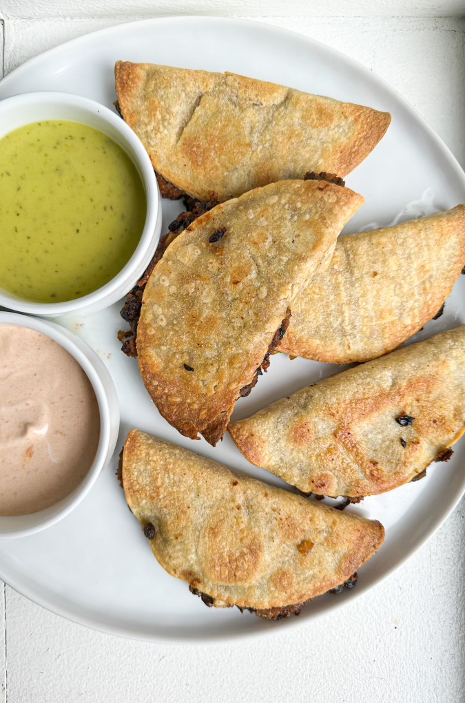 Crispy black bean tacos on a white plate with dipping sauces