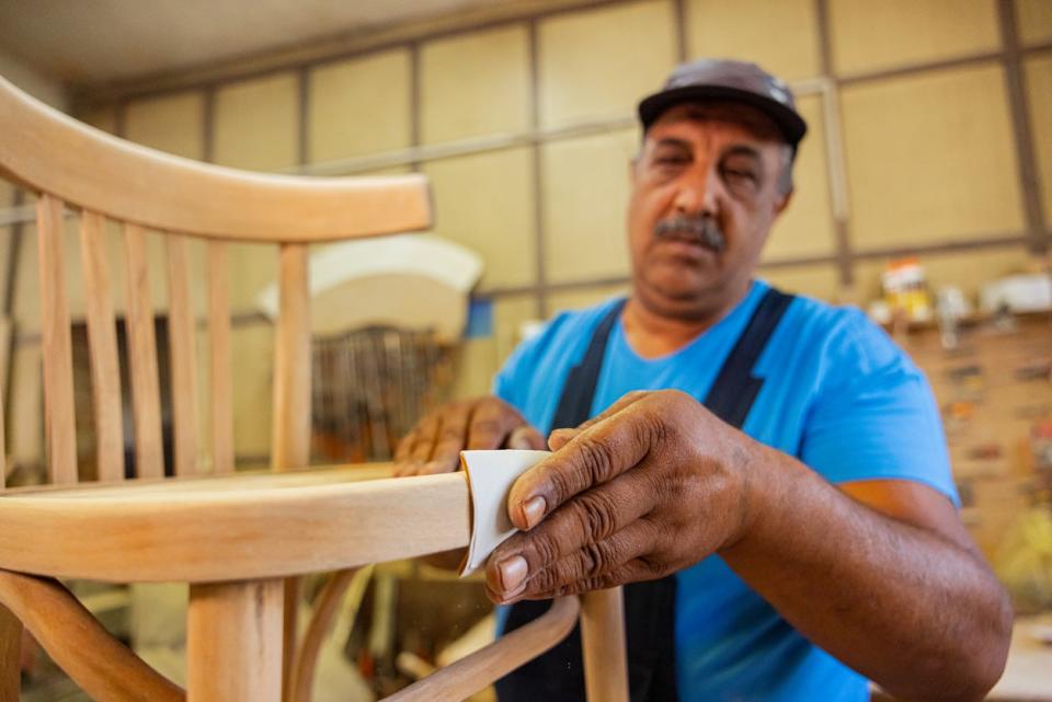 Carpenter sanding rough surfaces on a newly crafted wooden chair.