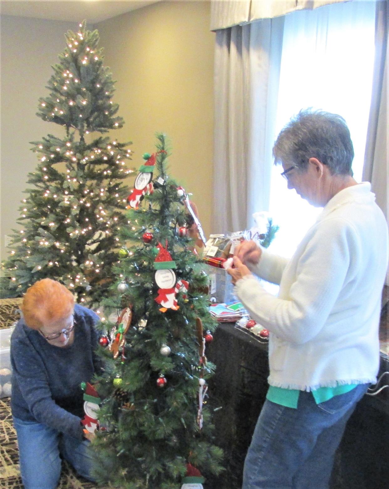 Emma Carpenter (left) and Ruth Hershberger, members of the Pomerene Hospital Auxiliary, help decorate and set up for the 12th Annual Christmas Tree Festival to be held at the Berlin Grande Hotel on Friday and Saturday.