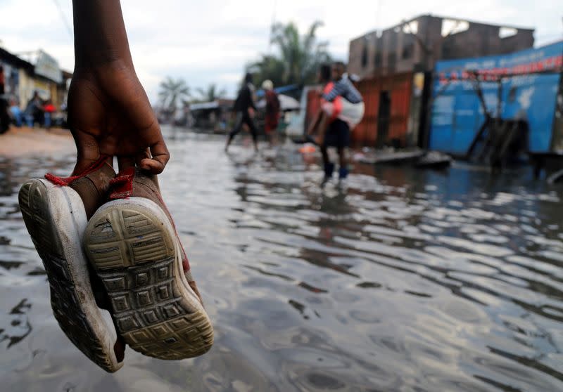 FILE PHOTO: A Congolese man carries his shoes as he wades through floodwaters along a street in Kinshasa