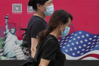 Women wearing face masks to help protect against the coronavirus walks by an advertising board displaying an American flag and Statue of Liberty on a street in Beijing, Thursday, Aug. 6, 2020. China's biggest recent outbreak of coronavirus has grown slightly. Hundreds people have developed COVID-19 in the far northwestern region of Xinjiang, with more than dozens of new cases reported Thursday in its capital and largest city, Urumqi. (AP Photo/Andy Wong)