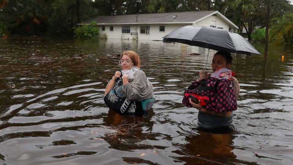 PHOTO: Makatla Ritchter (L) and her mother, Keiphra Line wade through flood waters after having to evacuate their home when the flood waters from Hurricane Idalia inundated it on Aug. 30, 2023 in Tarpon Springs, Fla. (Joe Raedle/Getty Images)