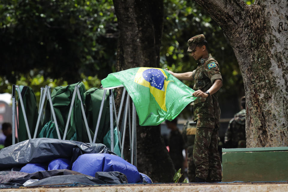 A soldier carefully collects national flags after supporters of former Brazilian former President Jair Bolsonaro left the encampment set up outside army headquarters in Brasilia, Brazil, Monday, Jan. 9, 2023, the day after Bolsonaro supporters stormed government buildings in the capital. (AP Photo/Gustavo Moreno)