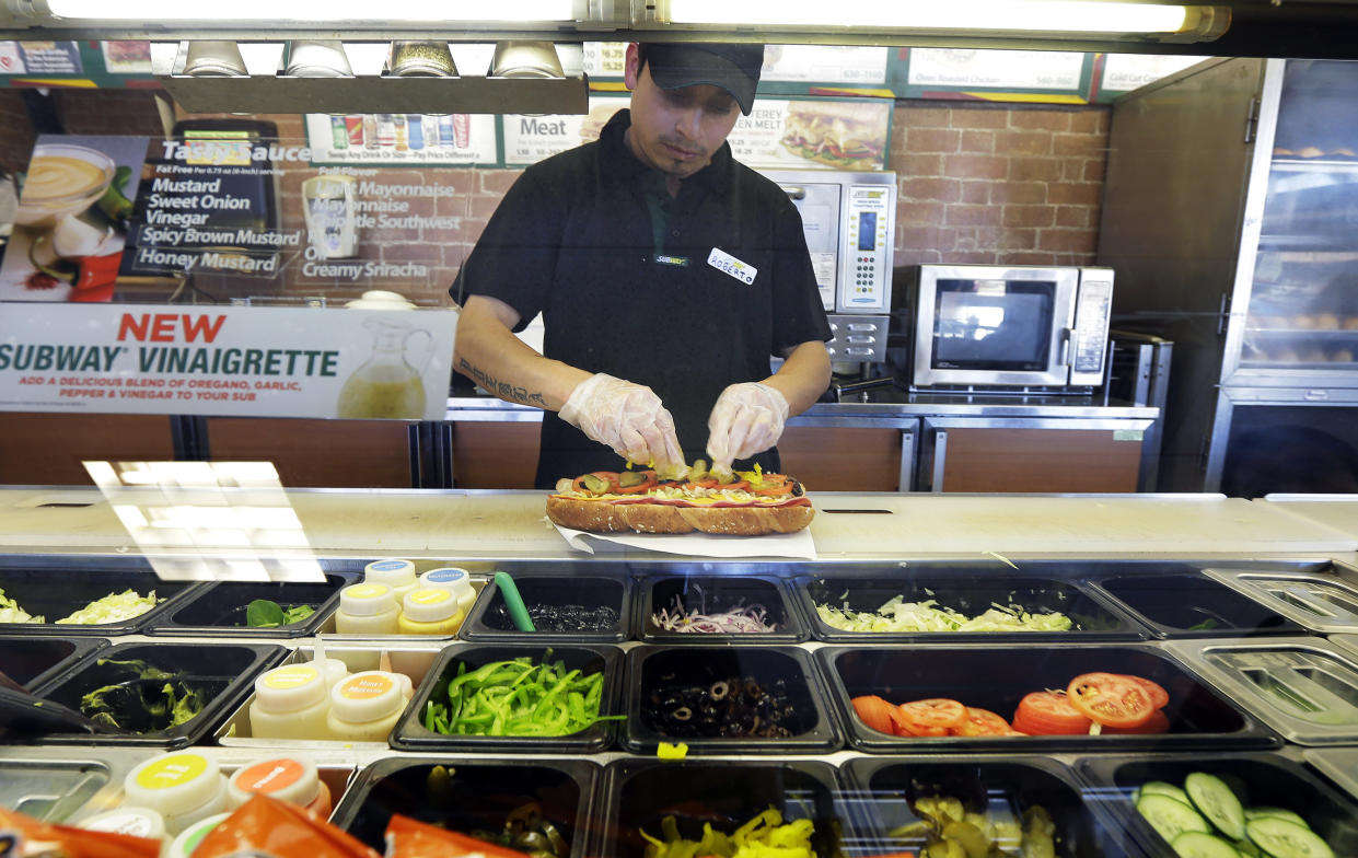 FILE- In this March 3, 2015, file photo, Roberto Castelan makes a sandwich at a Subway sandwich franchise in Seattle. Subway is changing up its loyalty program, letting customers earn $2 discounts instead of free Footlong sandwiches. The change, taking place in March 2018, is part of Subway’s plan to lure people back to the sandwich chain. (AP Photo/Ted S. Warren, File)