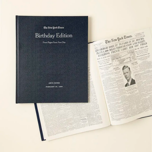 dark blue new york times birthday edition book laying on top of new york times newspaper