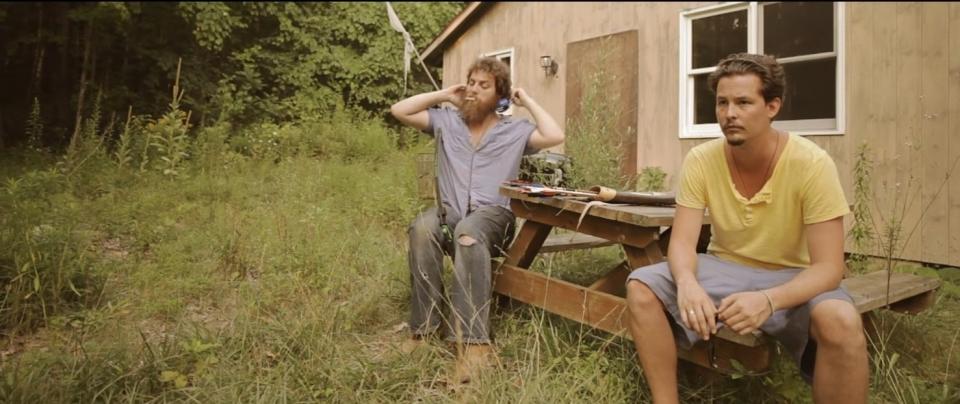 Two men sit patiently by an empty home on the edge of a forest