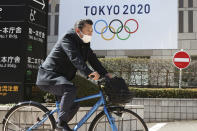 A man wearing a face mask cycles past the logo of the Tokyo Olympics, in Tokyo, Wednesday, Feb. 17, 2021. The Olympics are scheduled to open on July 23 but recent polls show about 80% of the Japanese public want the Olympics canceled or postponed. Gov. Tatsuya Maruyama of Shimane prefecture, western Japanese, is talking about canceling the torch relay events in his area for the Tokyo Games, reported on Wednesday. Maruyama is unhappy with COVID-19 prevention measures surrounding the relay. (AP Photo/Koji Sasahara)