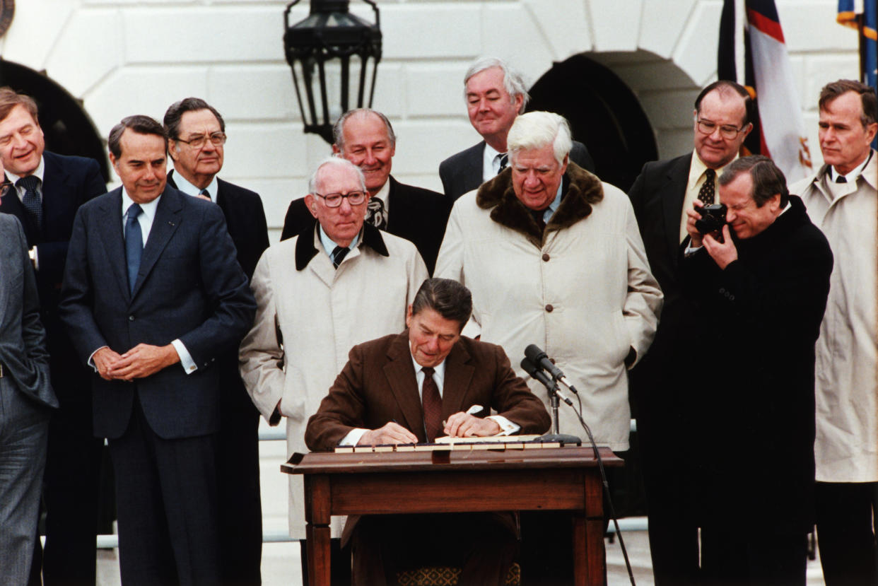 President Ronald Reagan signs the Social Security Act Amendment with Vice President George Bush (far r), Senator Bob Dole (2nd from l), and Congressmen Tip O'Neill (4th from r) and Daniel Moynihan (5th from r) on hand as witnesses. (Photo by © CORBIS/Corbis via Getty Images)