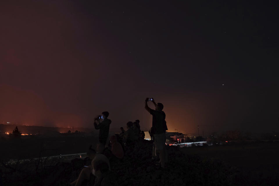 People take photos on their phones as a volcano continues to erupt on the Canary island of La Palma, Spain on Saturday Oct. 16, 2021. Officials say there is no sign that a volcanic eruption on the Spanish island of La Palma is coming to an end, one month after it began. The volcano on one of the Canary Islands off northwest Africa has so far destroyed more than 1,800 buildings, mostly homes. (AP Photo/Daniel Roca)