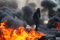 An Iraqi demonstrator walks next to burning tires blocking a road, during ongoing anti-government protests, in Kerbala