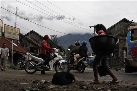 A villager walks carries her belonging as ash spews from Mount Sinabung at Payung village in Karo district, Indonesia's North Sumatra province December 1, 2013. REUTERS/Beawiharta