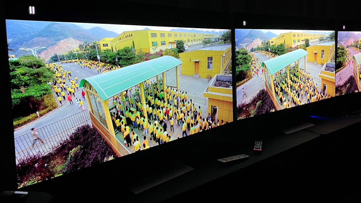  LG G3 and G2 OLED TVs in dark room with screen showing factory workers in yellow uniforms 