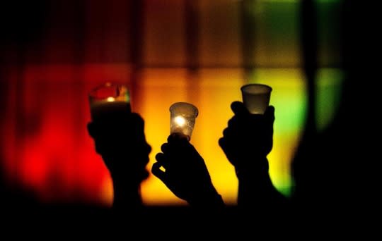 People hold up candles against a rainbow-lit backdrop during a vigil on Monday for those killed in a mass shooting at the nightclub Pulse in Orlando. (Photo: David Goldman/AP)