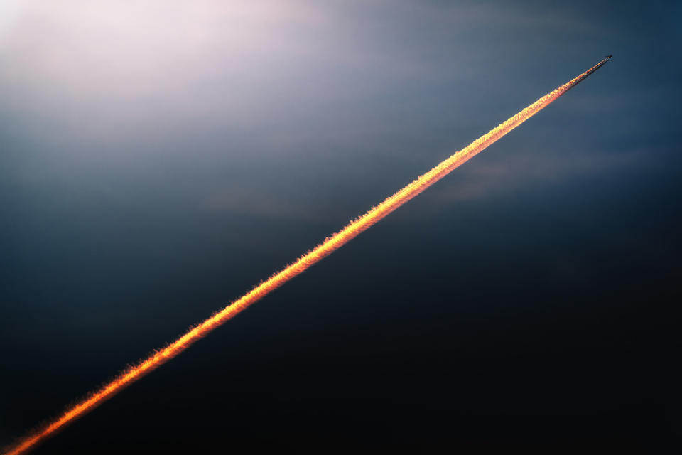 An airplane in high flight and the wake it leaves behind, colored by the sunset light and looking like a rocket