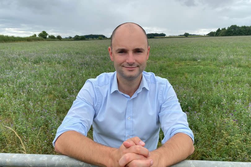 Man in light blue shirt leaning on a metal fence to a big field