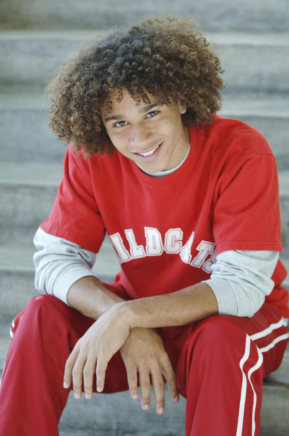 A smiling person sits in a relaxed pose wearing a casual red sports outfit