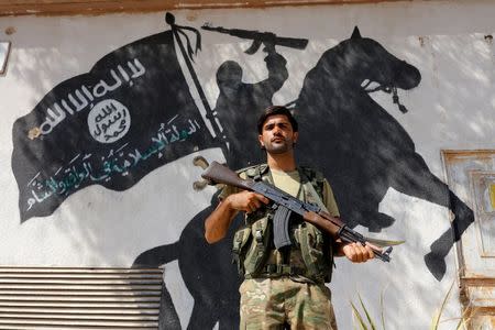 A member of Turkish-backed Free Syrian Army (FSA), seen with a mural of the Islamic State in the background, stands guard in front of a building in the border town of Jarablus, Syria, August 31, 2016. REUTERS/Umit Bektas