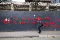 A man walks past anti-lockdown graffiti in Manchester, England, Monday, Oct. 19, 2020 as the row over Greater Manchester region's coronavirus status continues. Britain’s government says discussions about implementing stricter restrictions in Greater Manchester must be completed Monday because the public health threat caused by rising COVID-19 infections is serious and getting worse. (Peter Byrne/PA via AP)